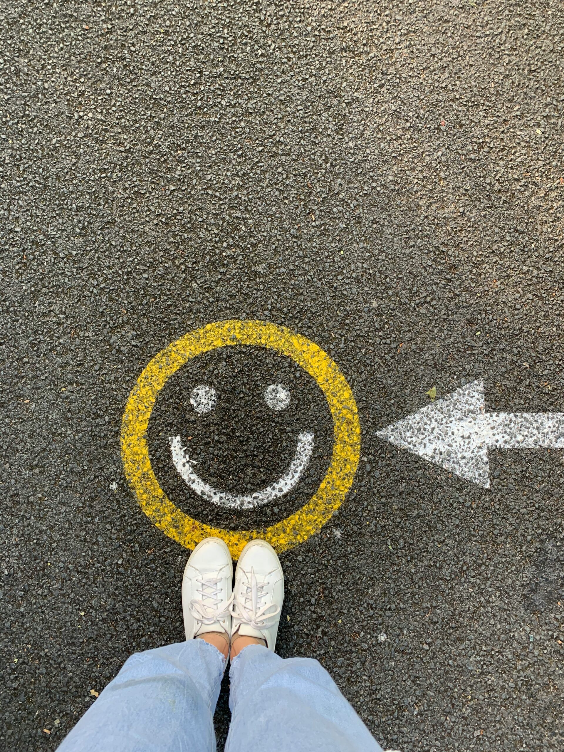 Smiley face on the ground with white arrow pointing towards it and somebody